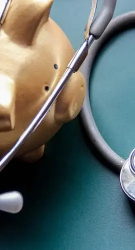 A golden piggy bank is juxtaposed with a stethoscope against a green background, symbolically representing the concept of financial health or the costs associated with medical care.