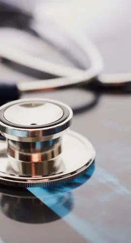 A stethoscope lies on a reflective surface alongside what appears to be a printed graph, suggesting a medical or healthcare setting.