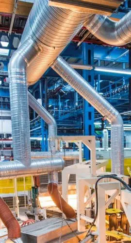 A modern industrial facility equipped with orange robotic arms and machinery, with a complex network of pipes overhead.