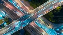 Aerial view of a busy, brightly lit freeway interchange at night with cars in motion.