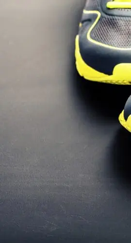 Pair of blue and yellow athletic shoes beside a plastic water bottle on a dark surface.