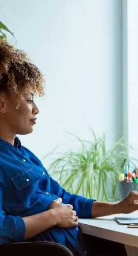 A person is working on a laptop at a desk with plants and office supplies nearby.