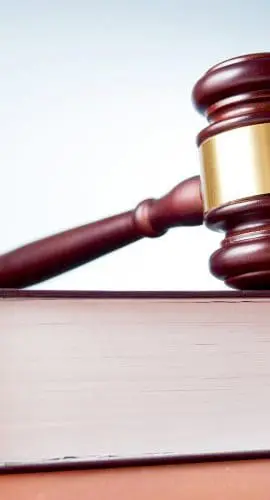 A gavel rests atop a closed book on a flat surface.
