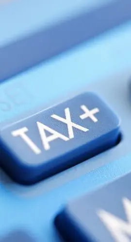 A close-up view of a blue calculator with a "TAX+" button prominently displayed.