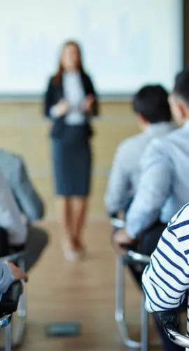 A professional speaker is giving a presentation to an attentive audience in a conference room.