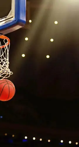 A basketball is mid-air heading towards a hoop during a game under bright lights.