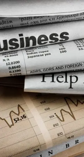 Stack of newspapers with headlines related to business and the economy.