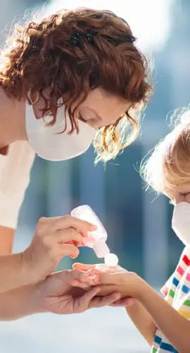 An adult is helping a child use hand sanitizer, and both are wearing masks.