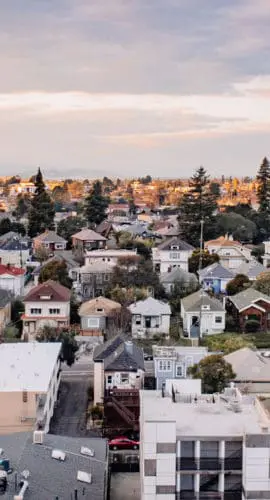 An aerial view showcases a suburban neighborhood with a mix of houses and trees under a partly cloudy sky.