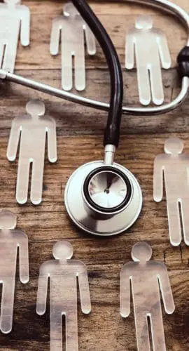 A stethoscope is laid over a wooden surface surrounded by transparent human figure cutouts.