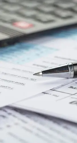 A pen and a calculator are placed on top of several tax forms.