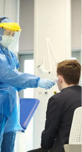 A healthcare worker in full protective gear is conducting a coronavirus test on a seated individual in a designated triage bay.