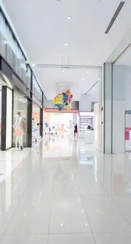 A modern, brightly lit shopping mall corridor with clothing stores and a clean, polished floor.