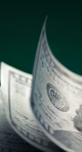 A stack of U.S. one hundred dollar bills with the top bill slightly curled.