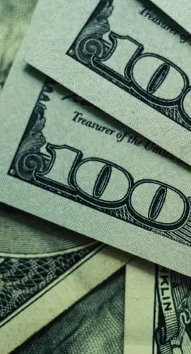 Several 100-dollar bills are fanned out, showing Benjamin Franklin's portrait.