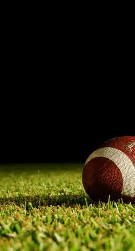 A football rests on a grassy field against a dark background.