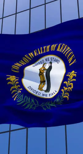 A Kentucky state flag is waving in front of a glass building.