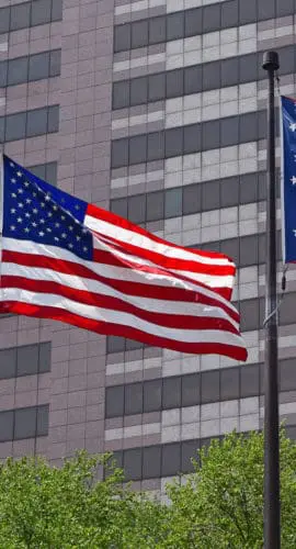 Two flags, one of the United States and one of Ohio, are flying in front of a tall building.