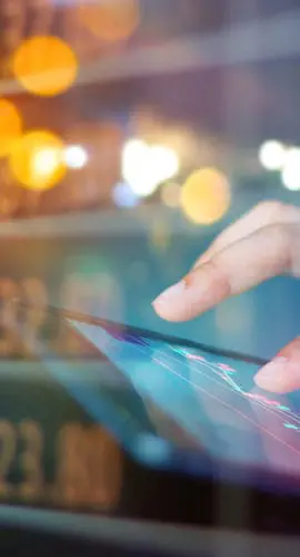 Hands operating a tablet with a digital stock market chart overlay displaying numerical data in the background.