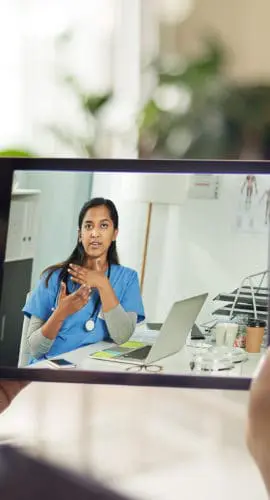 Someone is holding a tablet displaying a virtual medical consultation with a healthcare professional.