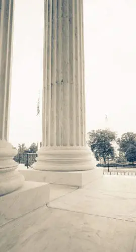 Large marble columns stand prominently with trees visible in the background.