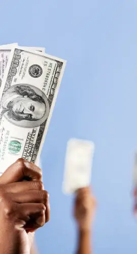 Multiple hands are holding up US dollar bills against a light blue background.