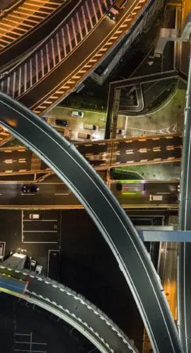 A complex network of illuminated highways and overpasses is captured from an aerial perspective at night.