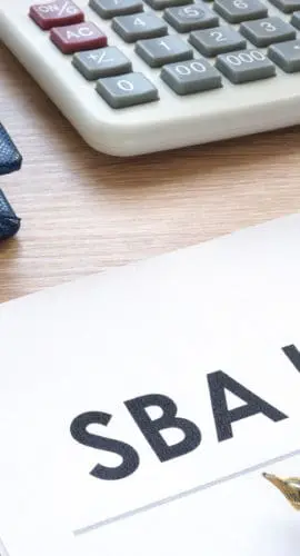 A document labeled "SBA loan" is on a desk next to a pen, some notebooks, and a calculator.