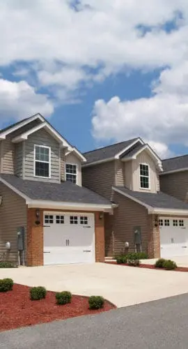 A row of suburban houses with manicured lawns and driveways are aligned under a partly cloudy sky.