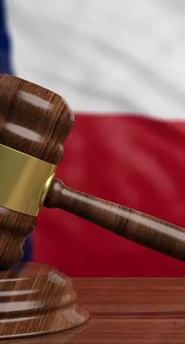 A gavel rests on a wooden table in front of a Texas flag.