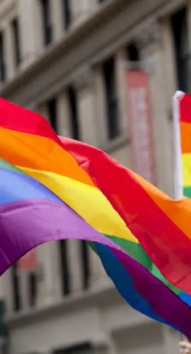 Rainbow flags are waving in front of a series of beige buildings.