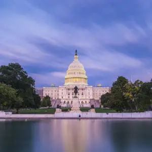The U.S. Capitol building is lit up against a twilight sky with a reflection on a calm body of water in the foreground.