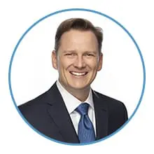 A smiling man in a suit and tie is framed within a blue circle.