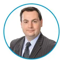 A man in a professional suit and tie is posed for a headshot within a blue circular border.