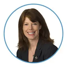 A person with long brown hair is smiling and wearing a dark blazer in a circular frame.