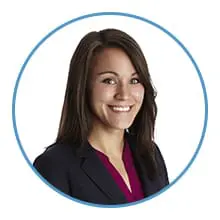 A woman with long brown hair, wearing a dark blazer over a maroon top, is smiling within a circular frame.