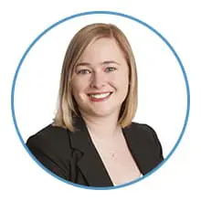 A smiling person with blonde hair is dressed in a black blazer within a circular blue border.