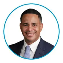 A man in a suit and tie smiles against a white background inside a blue circular frame.
