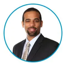 A person wearing a suit and tie is smiling against a white background, framed by a blue circle.