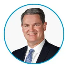 A man in a suit and tie is smiling inside a blue circular frame.