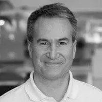 A smiling person is pictured in a grayscale photo, wearing a collared shirt.