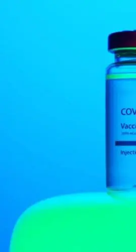 A vial labeled "COVID-19 Vaccine" is placed against a blue background.
