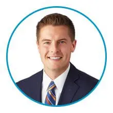 A man in a suit and striped tie is smiling within a blue circular frame.