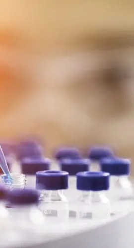 A person is using a pipette to transfer liquid into vials in a laboratory setting.