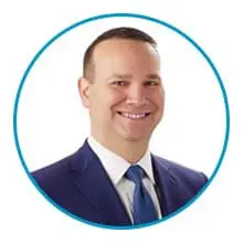 A smiling person in a suit and tie inside a blue circular border on a white background.