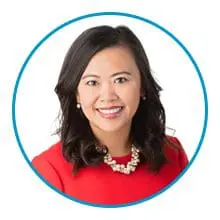 A woman with dark hair wearing a red top and a pearl necklace smiles, framed by a blue circle.