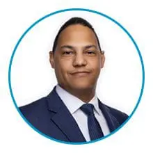 A person in a dark suit and tie, framed by a blue circle, is looking directly at the camera against a white background.