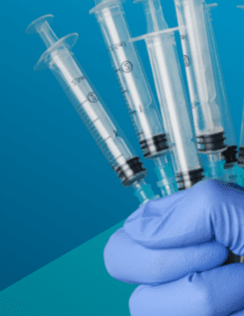 A gloved hand is holding several empty syringes against a blue background.