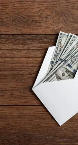 US dollars in a white envelope on a wooden table. The concept of income, bonuses or bribes. Corruption, salary, bonus.