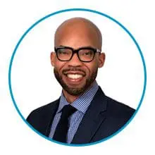 A man with glasses and a beard is smiling and wearing a suit and tie.
